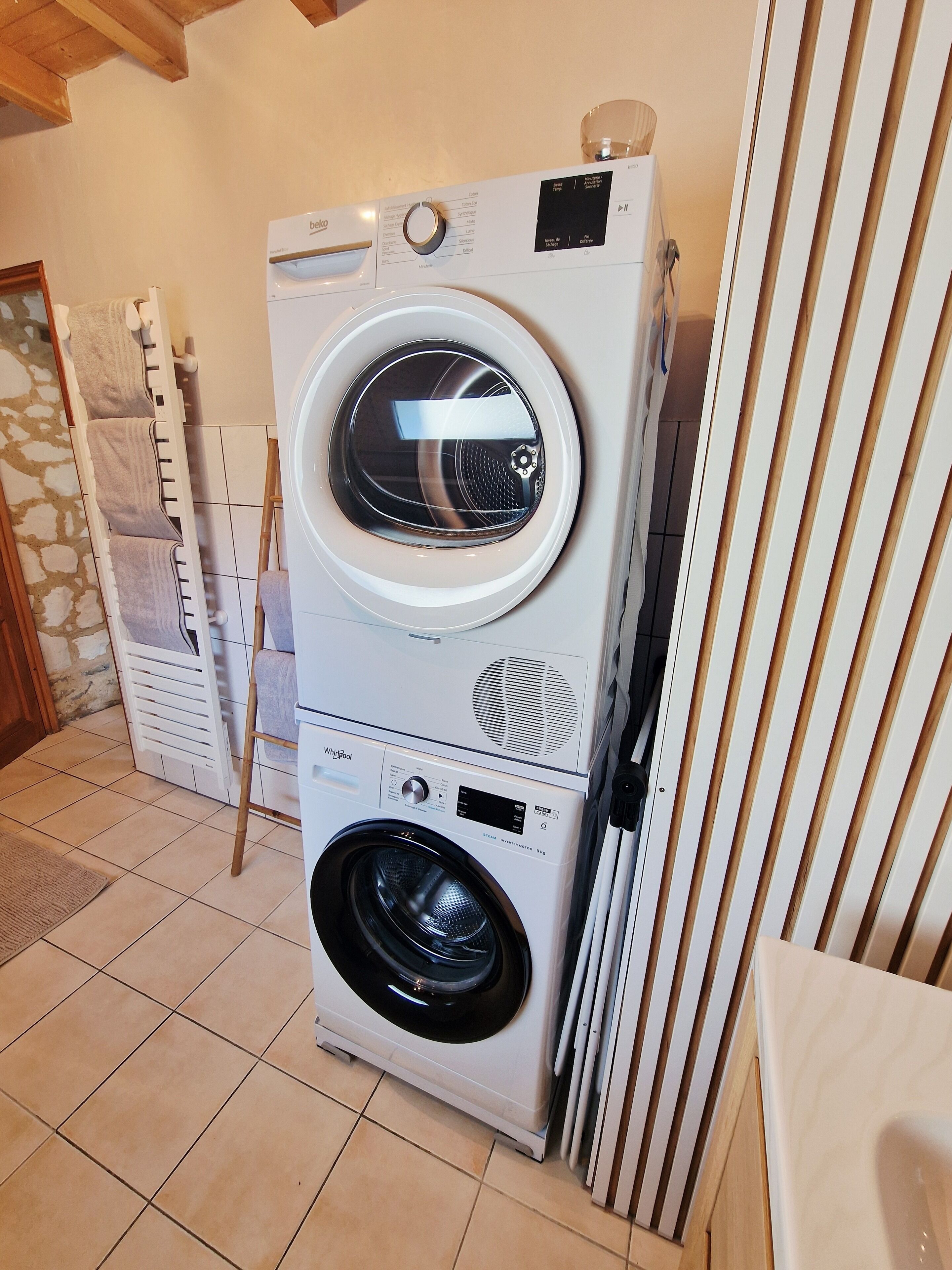 A stacked washer and dryer unit in a room with tiled flooring and a wooden ceiling.