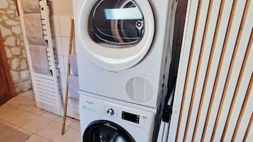 A stacked washer and dryer unit in a room with tiled flooring and a wooden ceiling.