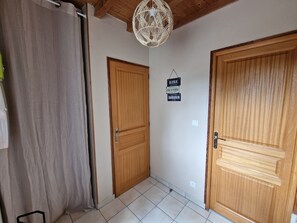 Een kamer met twee houten deuren, een vloer van witte tegels en een hanglamp.