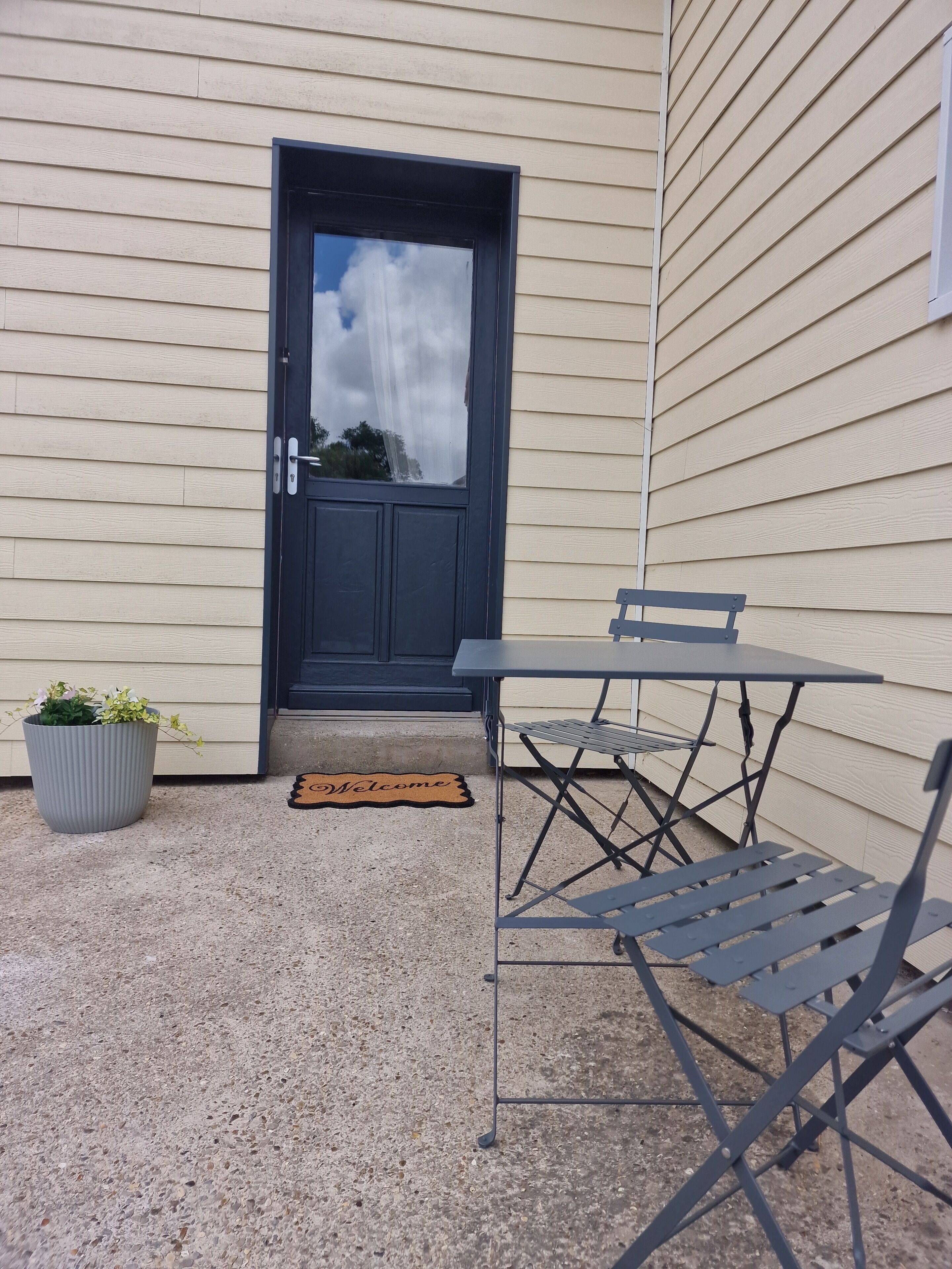 Et udendørs siddeområde med et bord, stole, en potteplante og en velkomst måtte.