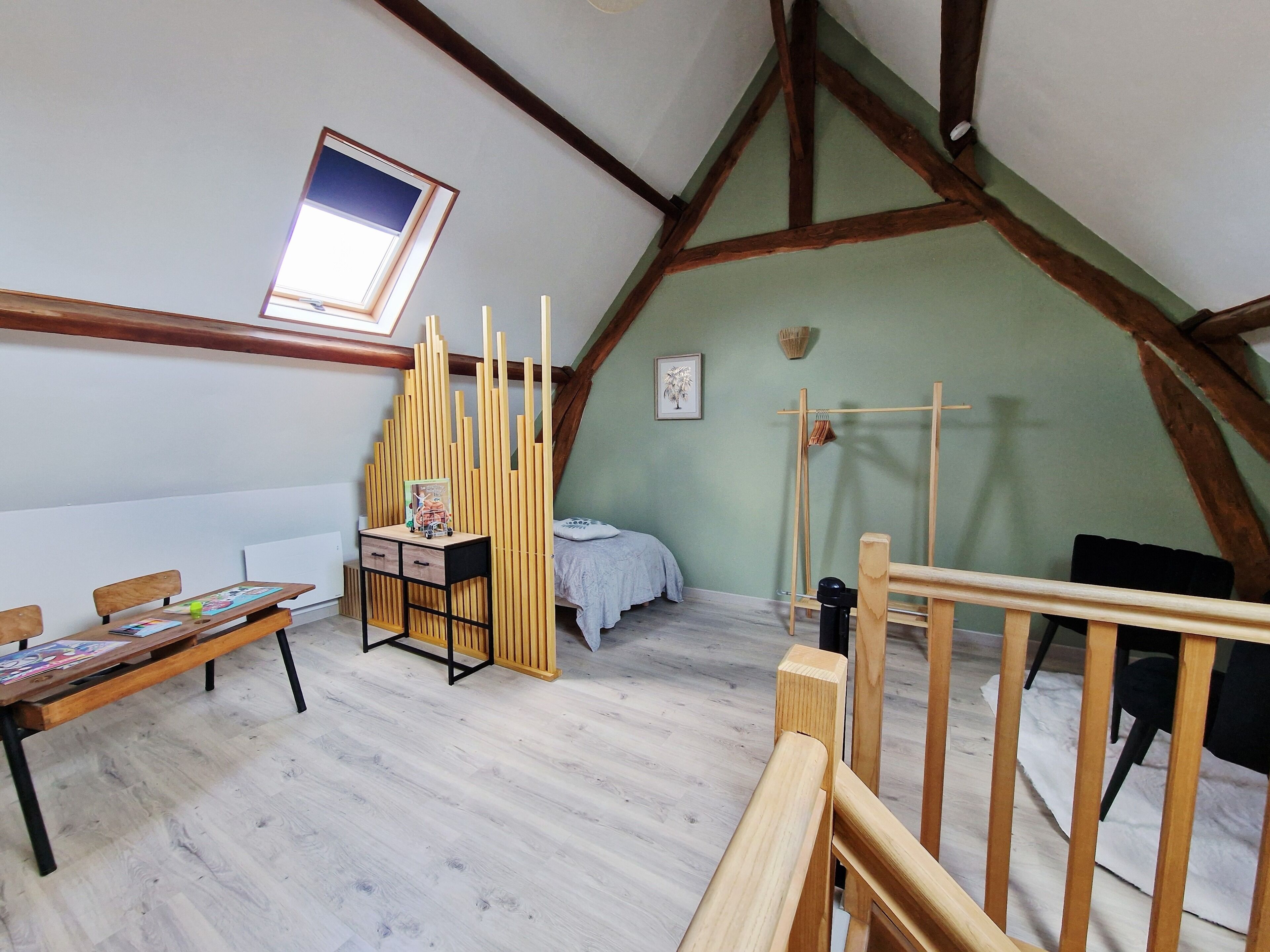 Una habitación con techo inclinado, un escritorio de madera con cajones, una cama con colcha blanca y una ventana con vistas.