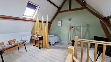 Una habitación con techo inclinado, un escritorio de madera con cajones, una cama con colcha blanca y una ventana con vistas.
