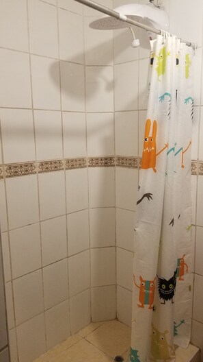 A shower area with a white tiled wall, a showerhead, and a curtain with cartoon characters. - Charming 3-bedroom apartment in the heart of Cusco (Cusco)