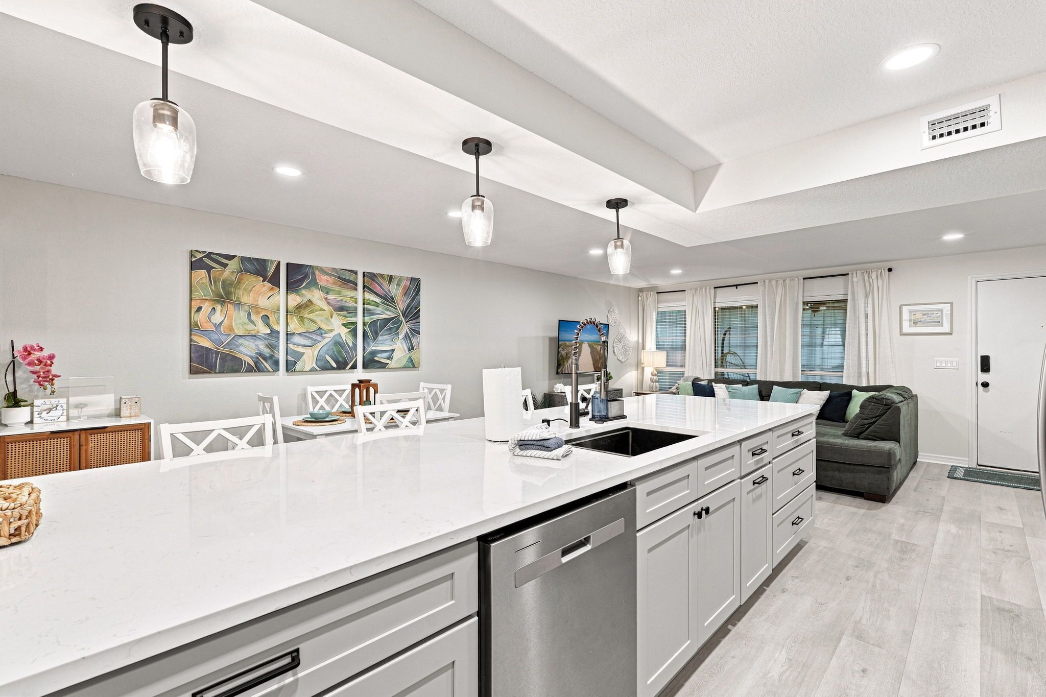A modern kitchen with a large island, pendant lighting, and a dining area with a sofa.