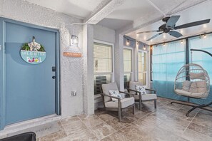 A room with a blue door, a sign reading 'Mad Beach', two chairs, a hanging chair, and a ceiling fan. - The Seashell Sanctuary, Poolside, Sleeps 8, Beach, Boat Slip, cable & wifi (Madeira Beach)