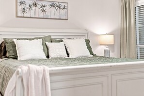 Ein ordentlich bezogenes Bett mit einer grün-weißen Tagesdecke, einer weißen Zierdecke und grünen Kissen.
