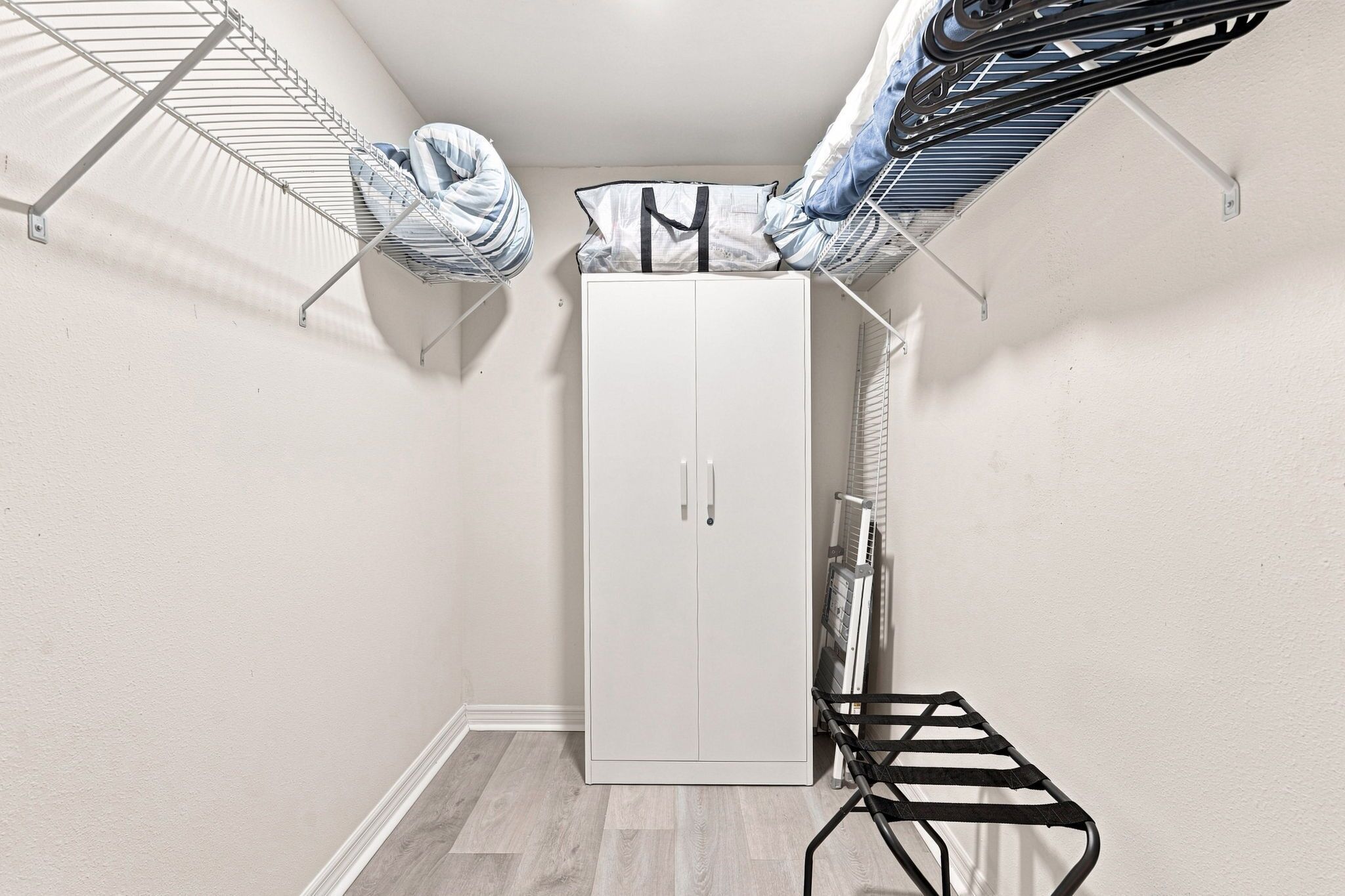 Ein Zimmer mit einem weißen Kleiderschrank, einem Wäscheständer und einem schwarzen Stuhl.