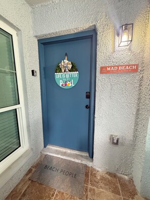 A blue door with a life is better by the pool sign, a 'Mad Beach' sign, and a 'Beach People' mat. - The Seashell Sanctuary, Poolside, Sleeps 8, Beach, Boat Slip, cable & wifi (Madeira Beach)