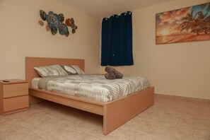 A bedroom with a bed, a nightstand, a wall decoration, a painting, and a curtain. - Family Rainforest Escape House (Río Grande)