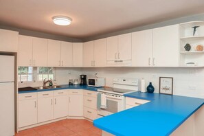 A kitchen with white cabinets, a blue countertop, a stove, a microwave, and a sink. - Family Rainforest Escape House (Río Grande)