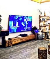 A modern living room with a flat-screen TV mounted on the wall, a wooden bench, and a decorative shelf with various items.