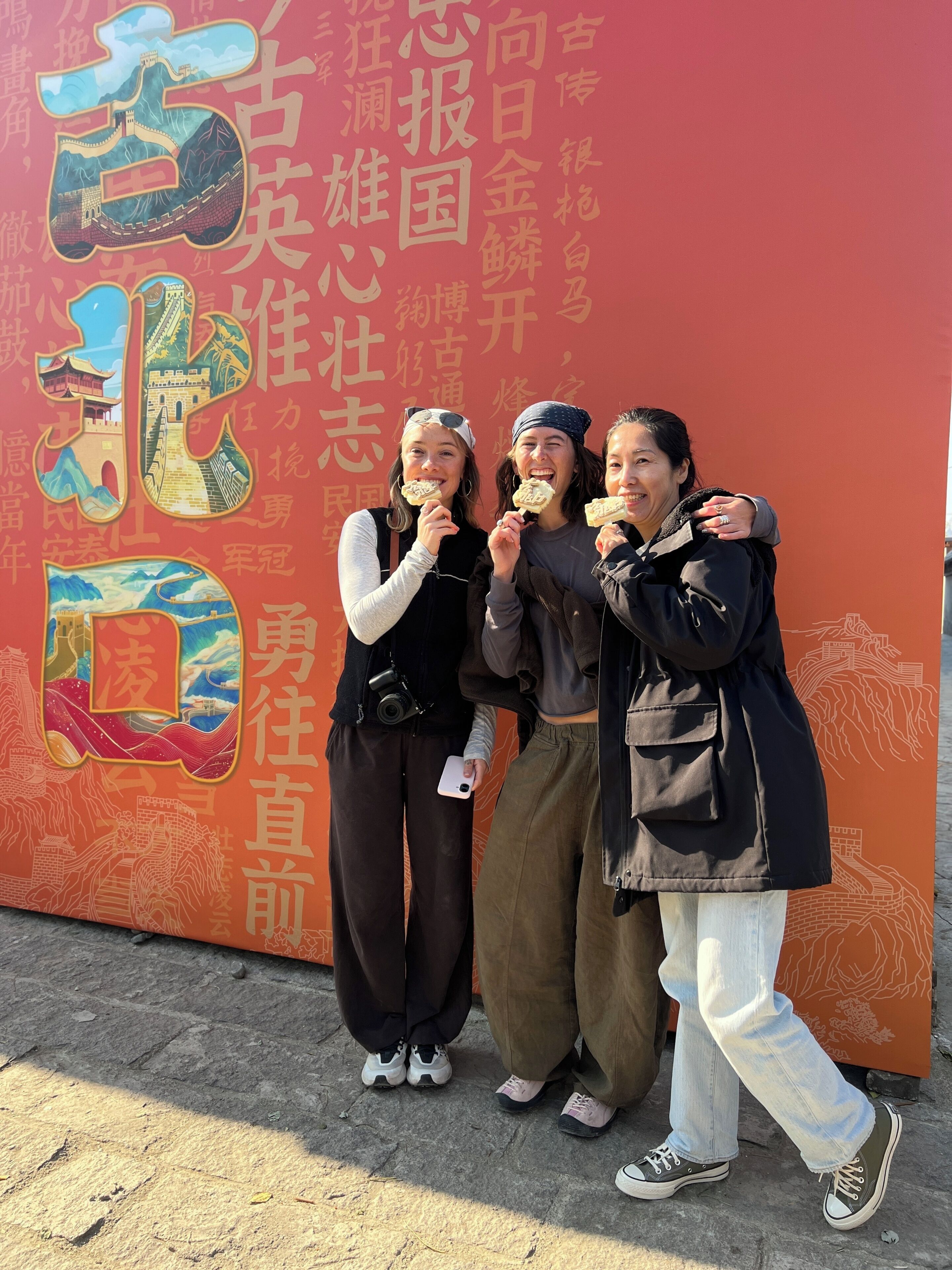 Un grupo de personas frente a un muro con grandes caracteres e ilustraciones chinas.