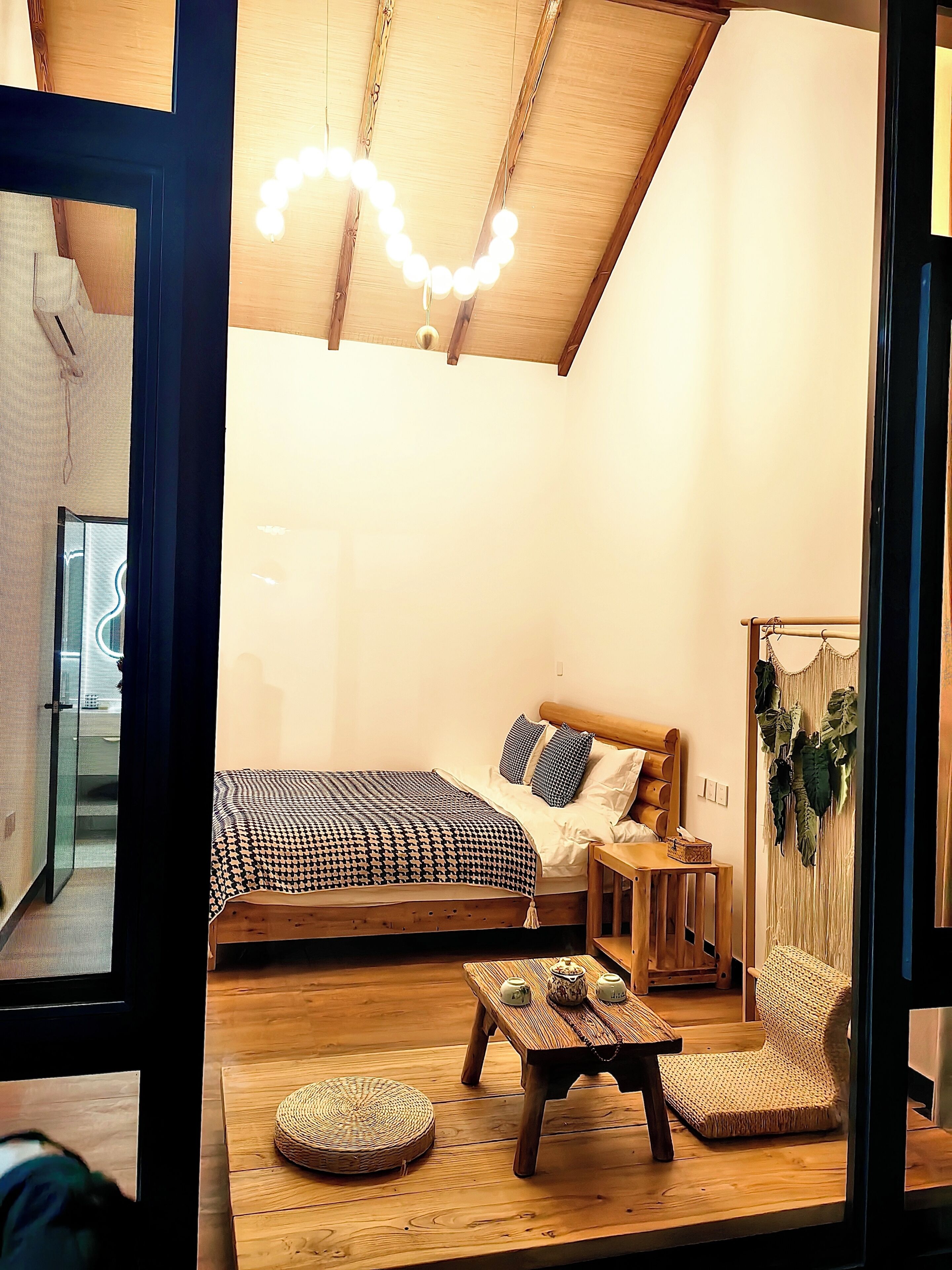 A cozy bedroom with a wooden ceiling, a bed with patterned bedding, a bedside table, and a small wooden table with decorative items.