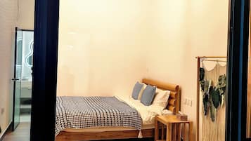 A cozy bedroom with a wooden ceiling, a bed with patterned bedding, a bedside table, and a small wooden table with decorative items.