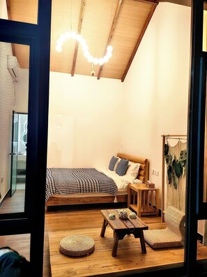 A cozy bedroom with a wooden ceiling, a bed with patterned bedding, a bedside table, and a small wooden table with decorative items.