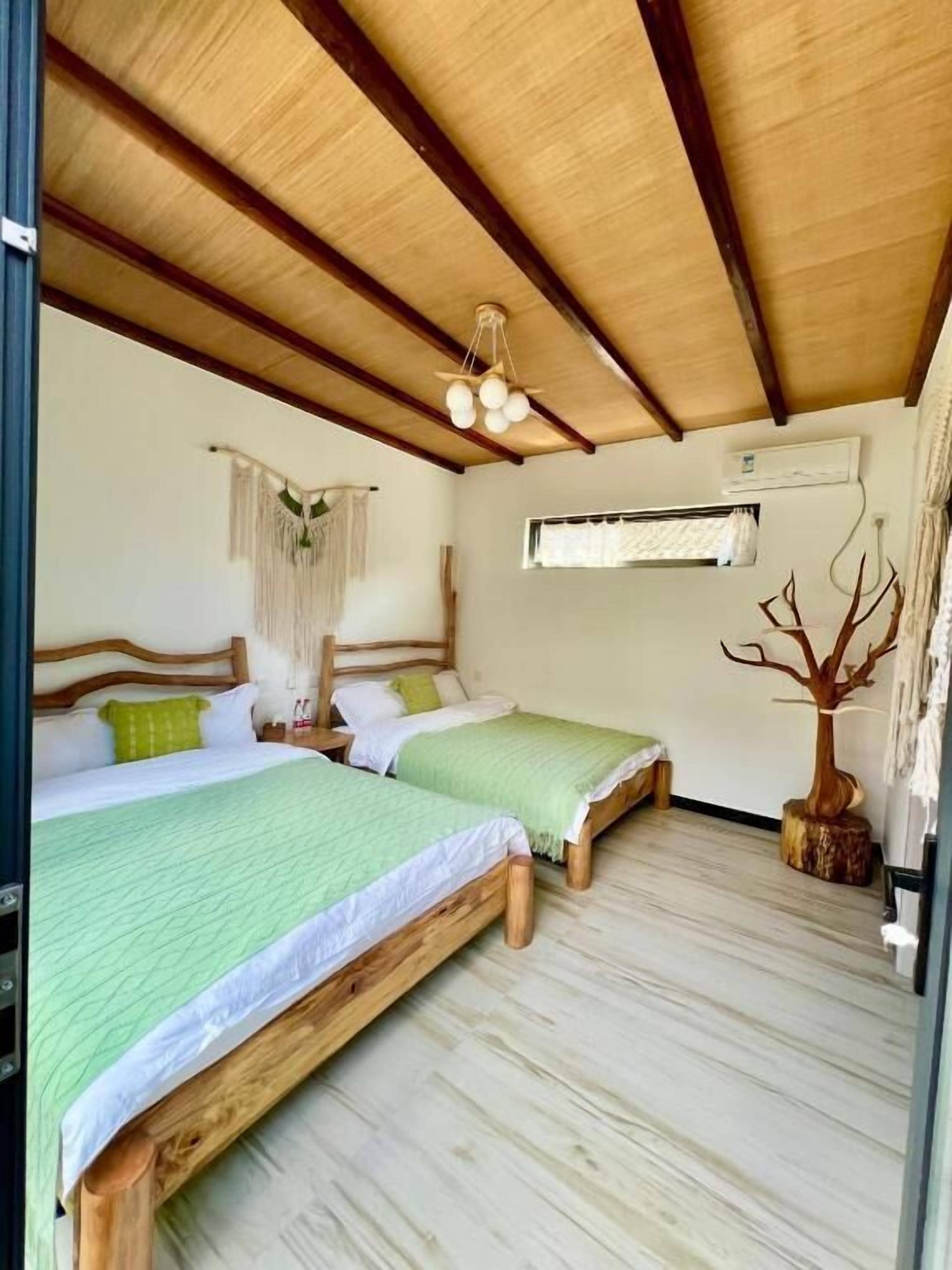 Una habitación con dos camas de madera, un ventilador de techo, aire acondicionado de pared y una planta decorativa.