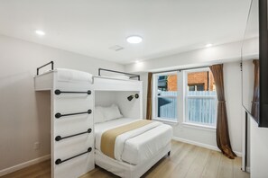 A room with bunk beds, a window with curtains, and a bed with a beige blanket. - Cowboy Oasis | Sleeps 7 (Houston)