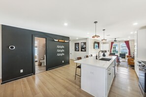 A modern kitchen with a central island, a dining area with chairs, and a living space with a sofa and a TV. - Cowboy Oasis | Sleeps 7 (Houston)