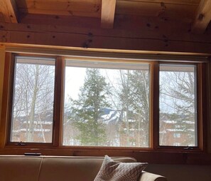 Ein Zimmer mit großem Fenster, Holzbalkendecke und einer Couch mit Kissen.