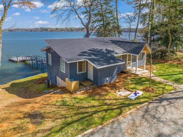 Une cabane à deux étages avec un quai, entourée d’arbres et bordant un lac.