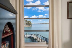 A view through a window with a wooden dock extending into a calm body of water, surrounded by trees and a clear sky. - ★ LAKE NORMAN WATERFRONT COTTAGE, PETS ALLOWED ❤ DOCK + KAYAKS w/FIRE PIT (Lake Norman of Catawba)