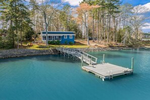 Uma cabana à beira do lago com um cais que se estende sobre a água, rodeada por árvores.