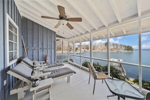 Uma sala de sol com vista para um lago, mobiliada com um sofá, cadeiras e uma mesa.