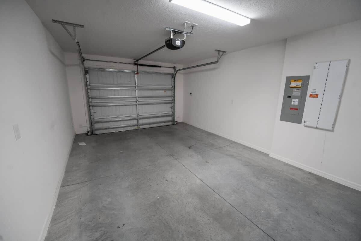 Un garage doté d’une porte métallique fermée, d’un projecteur fixé au plafond et d’une boîte de raccordement électrique sur le mur.