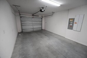 Ett garage med en stängd metalldörr, en projektor som är monterad i taket och en elcentral på väggen.