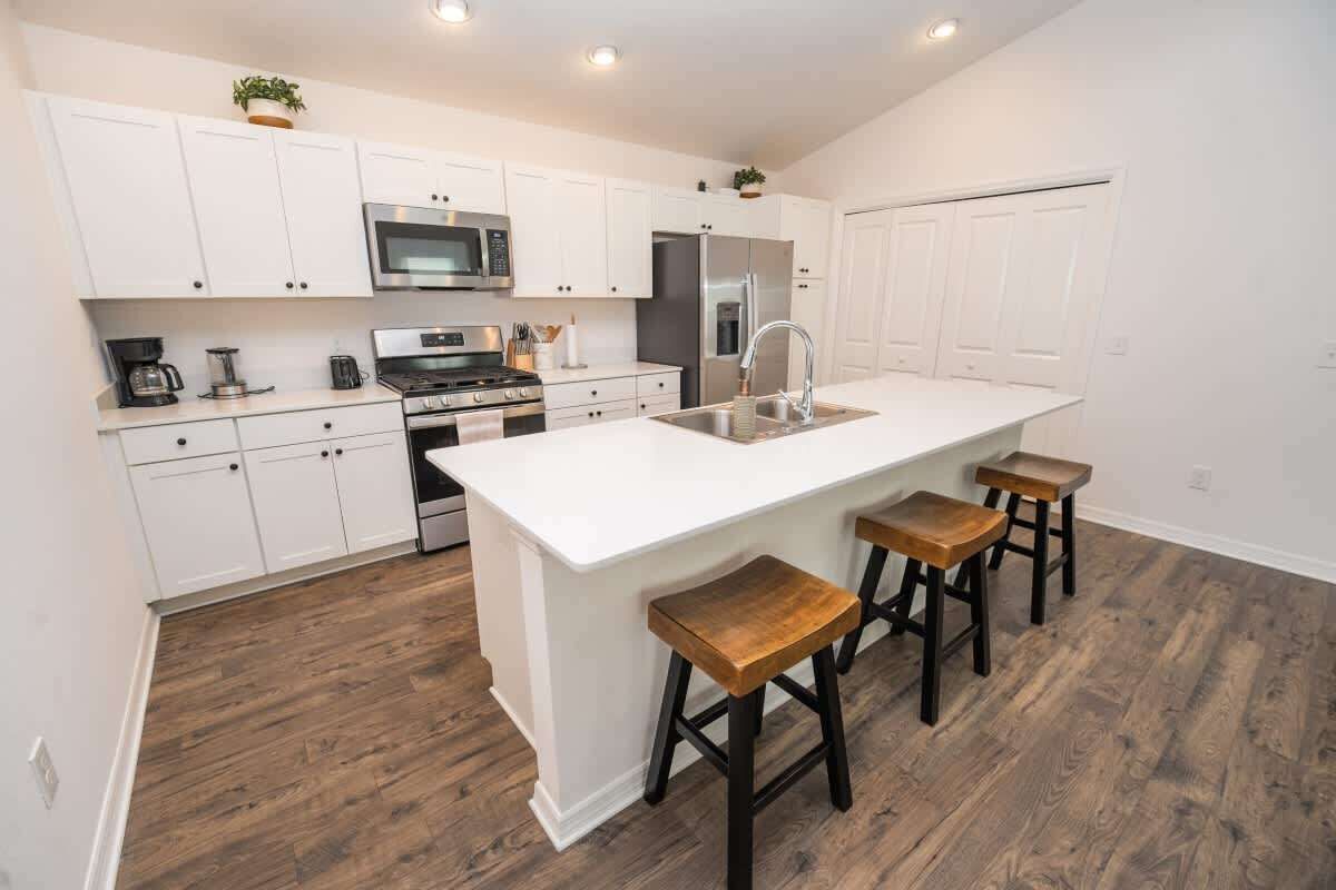 A modern kitchen with white cabinetry, a central island with stools, stainless steel appliances, and a wooden floor.