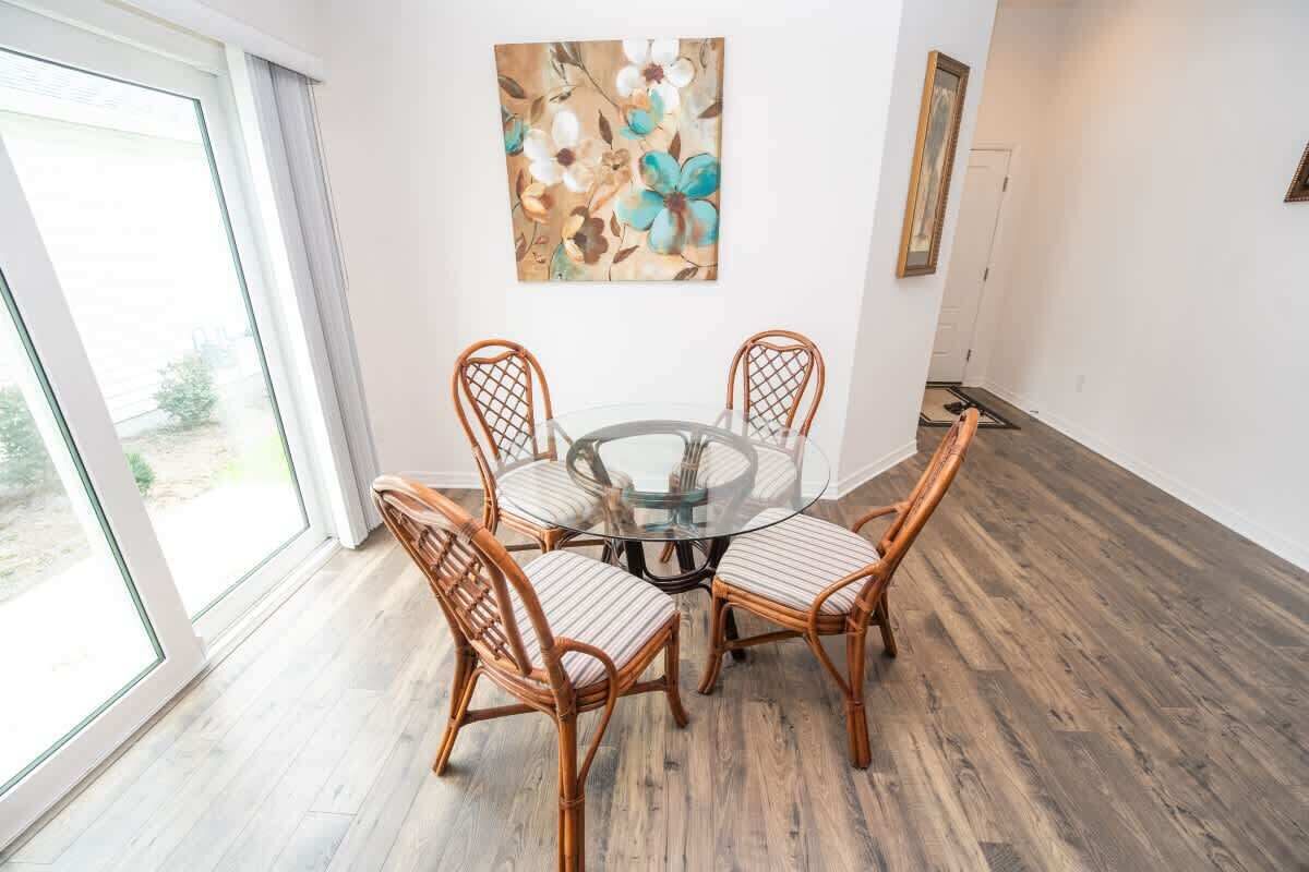 A dining area with a glass table surrounded by wicker chairs, a painting on the wall, and a view through a glass door.