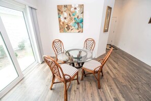 A dining area with a glass table surrounded by wicker chairs, a painting on the wall, and a view through a glass door. - 5 minutes to EastPort, Life Style ID's! (Sumterville)
