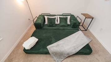 A bed with a green cover, a grey blanket, and white pillows.