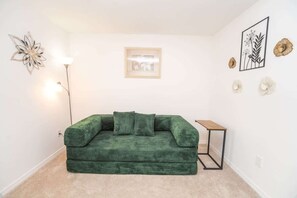 Ein grünes Sofa in einem Raum mit einem gerahmten Bild an der Wand, einer Stehlampe und dekorativer Wandgestaltung.