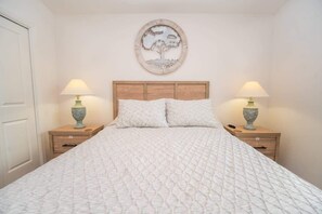 A bedroom with a bed, two bedside tables with lamps, a wooden headboard, and a wall-mounted artwork.