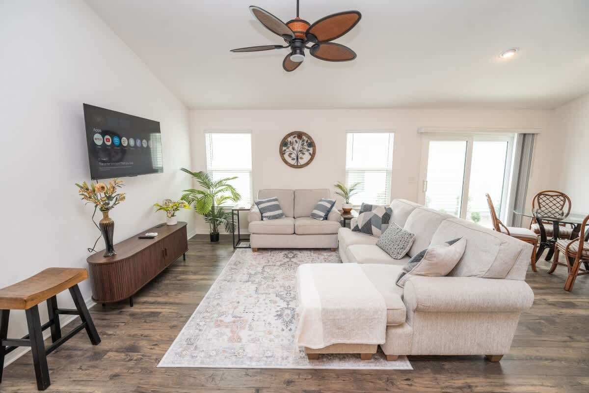 A living room with a sofa, a coffee table, a TV mounted on the wall, and a ceiling fan.