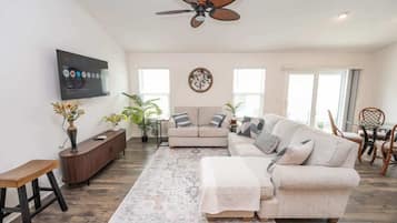 A living room with a sofa, a coffee table, a TV mounted on the wall, and a ceiling fan.