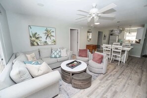 A living room with a sofa, coffee table, and ottoman, a dining area with chairs, and a kitchen in the background. - Private Pool, 2 Seater Golf Cart, Life Stlye ID's (Lady Lake)