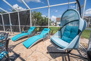 A covered outdoor area with a swing chair and lounge chairs. - Private Pool, 2 Seater Golf Cart, Life Stlye ID's (Lady Lake)