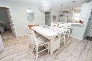 A dining area with a white table and chairs, a hanging light fixture, and a kitchen in the background. - Private Pool, 2 Seater Golf Cart, Life Stlye ID's (Lady Lake)