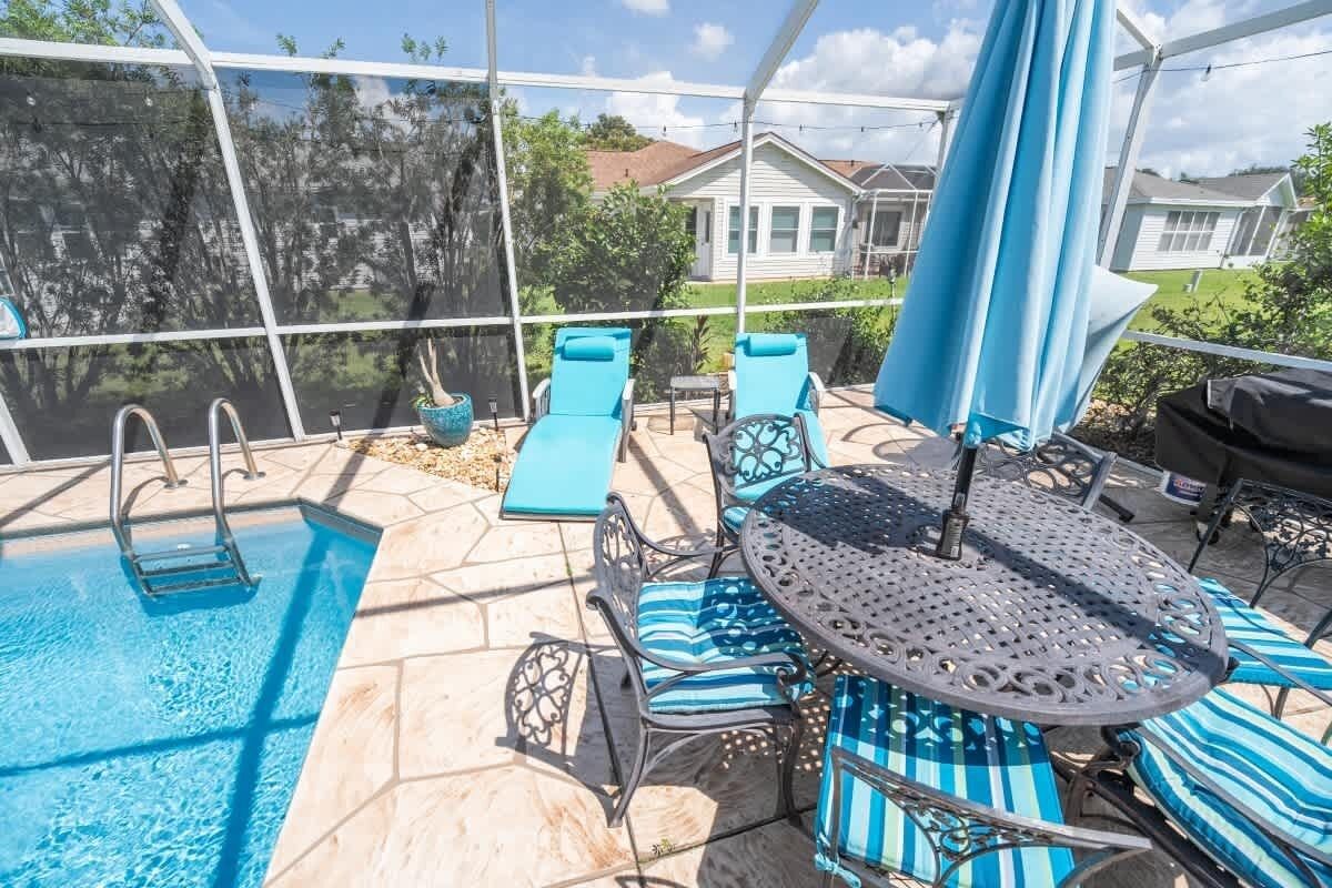 Un espace extérieur avec une piscine, une table et des chaises, un coin salon abrité et une vue sur une maison en arrière-plan.