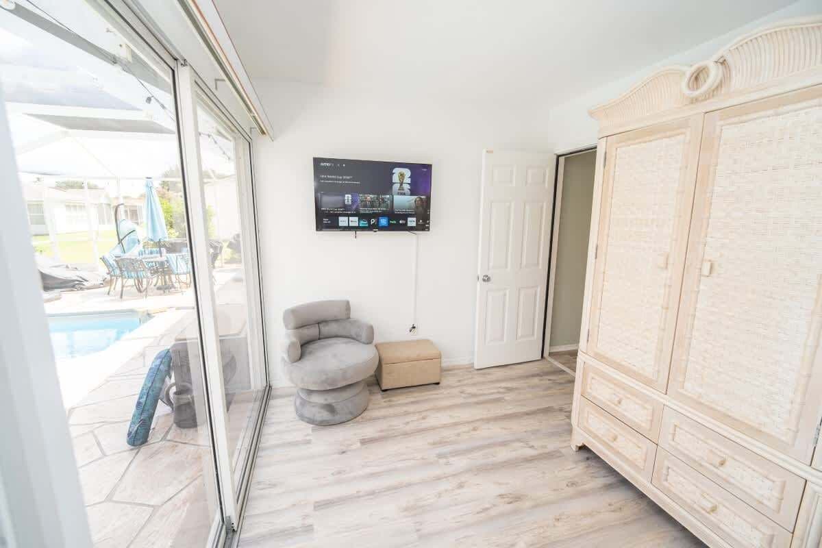 Habitación con vista a la piscina, un sillón gris, un televisor montado en la pared y un armario blanco grande.