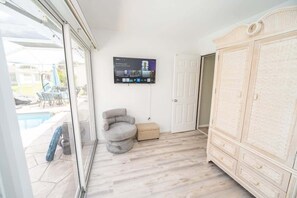 A room with a pool view, a grey armchair, a television mounted on the wall, and a large white wardrobe. - Private Pool, 2 Seater Golf Cart, Life Stlye ID's (Lady Lake)