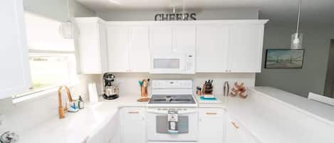 Una cocina con armarios blancos, un microondas, un horno y un ventilador de techo.