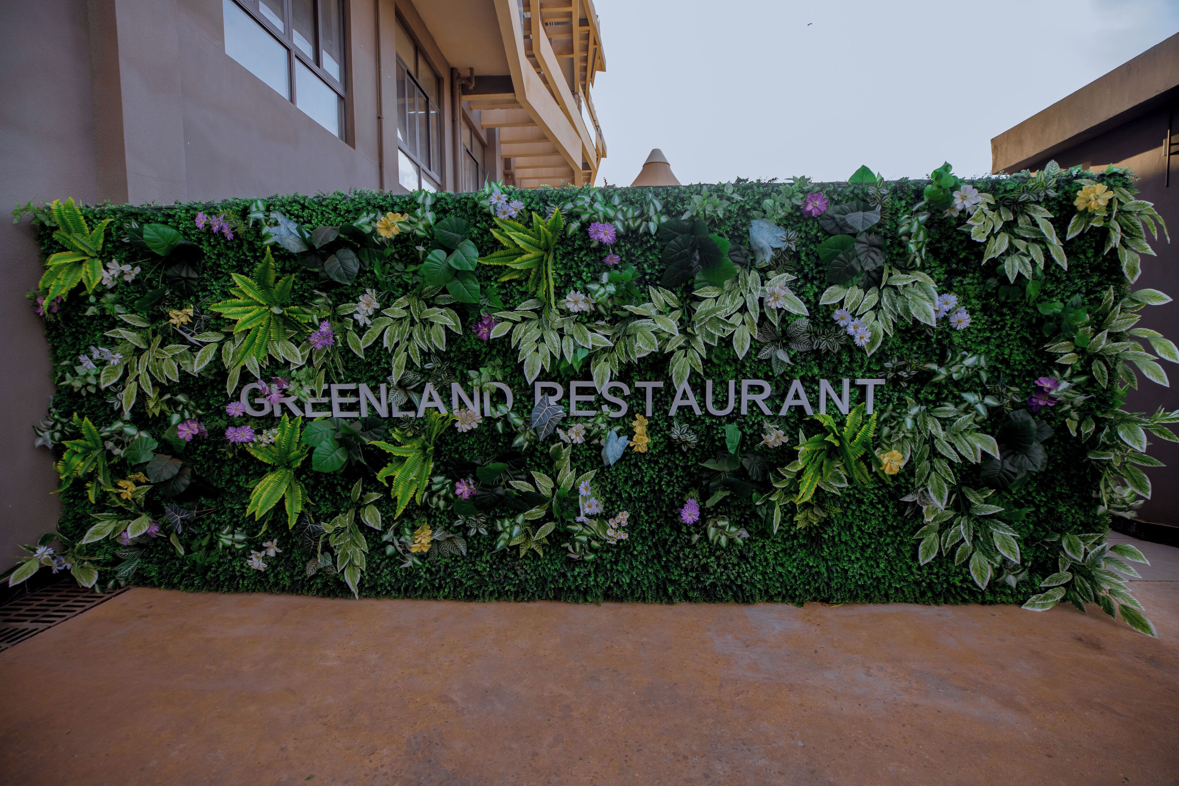 Een muur met diverse planten en de tekst 'GREENLAND RESTAURANT', wat duidt op een restaurant.