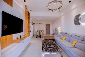 Una sala de estar moderna con un televisor de pantalla plana, un sofá con cojines, una mesa de centro y un comedor con sillas.