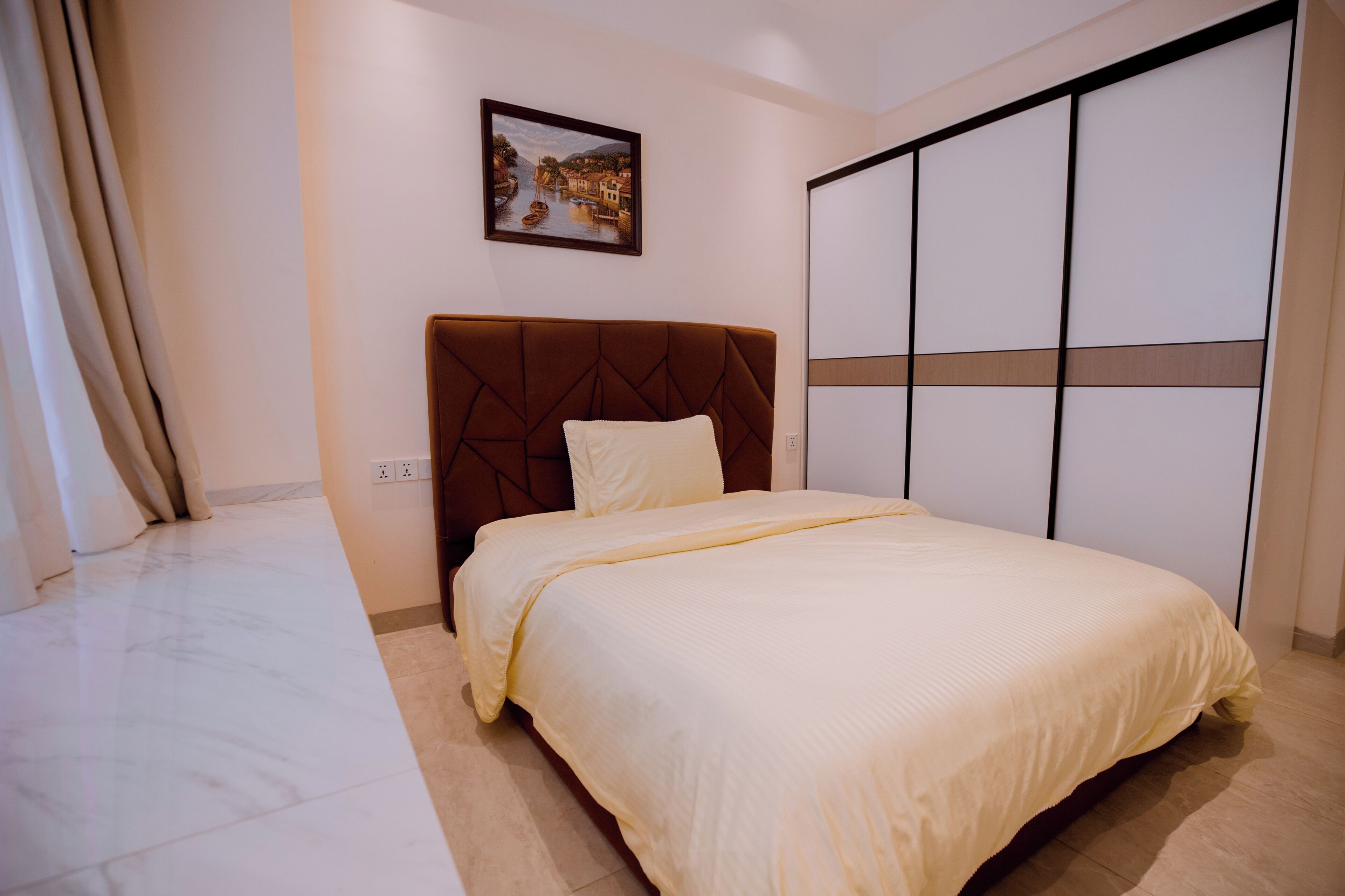 Un dormitorio con cama, cabecera, un cuadro en la pared y una puerta corrediza.