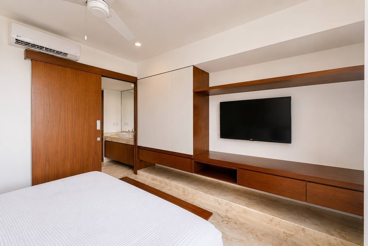 A modern bedroom with a bed, a TV mounted on the wall, a wardrobe, and a mirror.