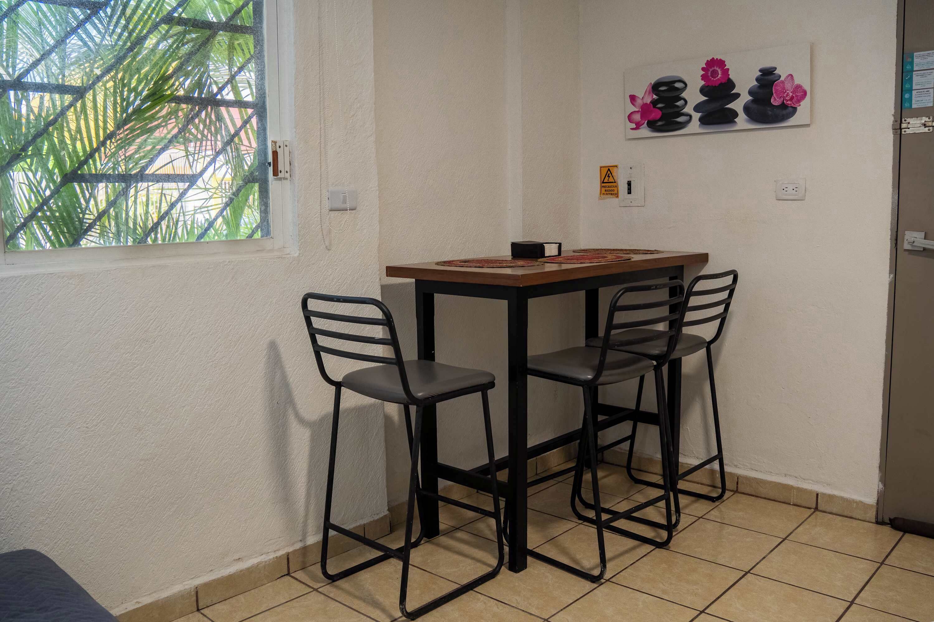 A small room with a table and two chairs, a window with a view of greenery, and a wall-mounted artwork.