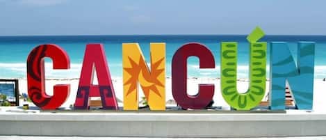 Letras grandes e coloridas formando a palavra 'CANCÚN' em uma praia, com o oceano ao fundo.